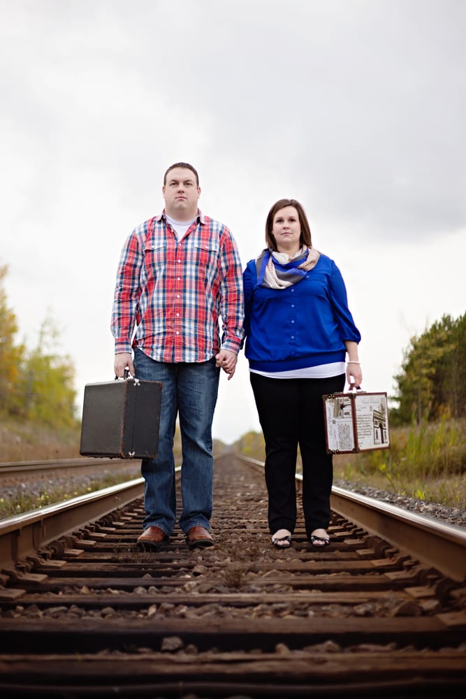 Cornwall engagement session - couple standing on train track with suitcases