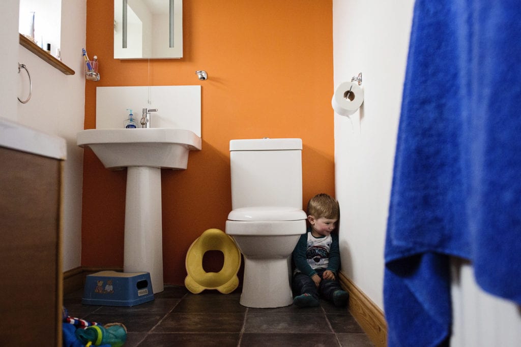 boy hiding next to toiletduring session with Wales family photographer