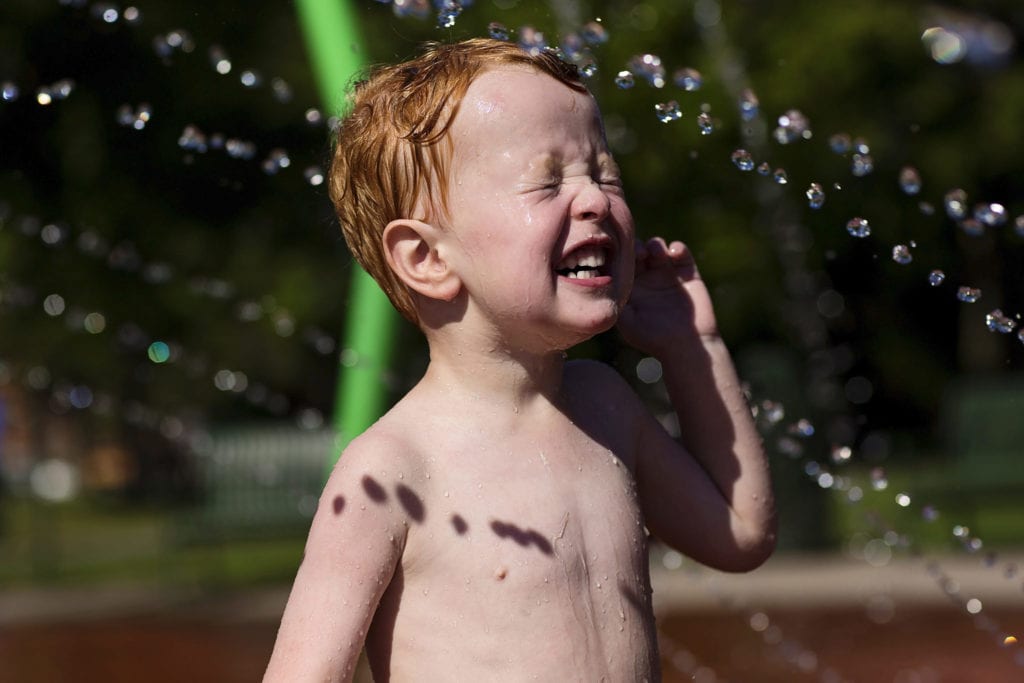 red-headed boy being splashed in face with water during Modern Cornwall family photography session