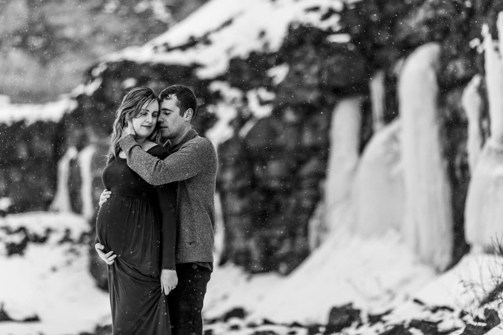 man holds pregnant wife in front of icy backdrop during winter Cornwall maternity session