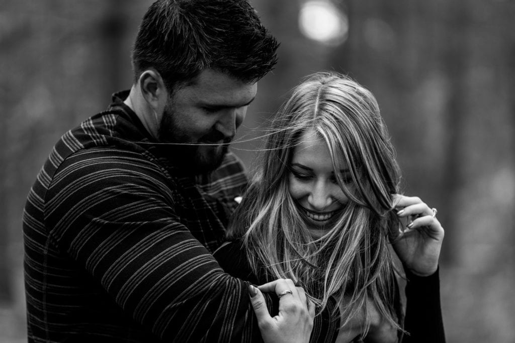 woman with hair blowing around face is held by fiance