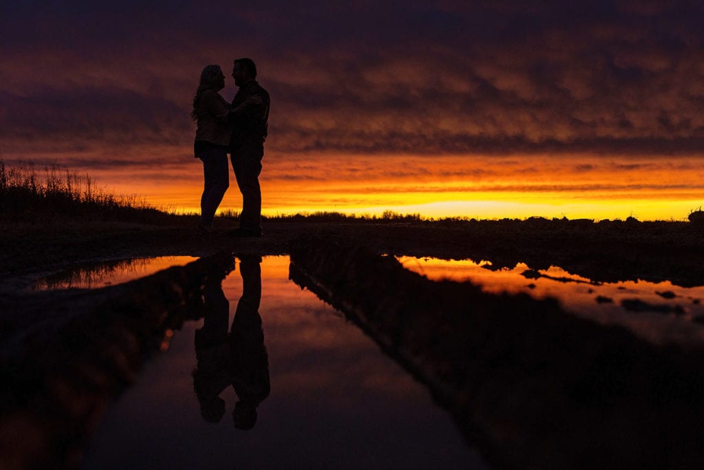 couple silhouetted in puddle and against red orange and pink sky