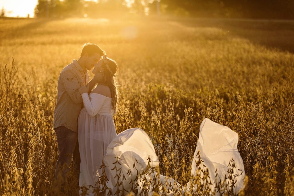 man leans in to kiss pregnant woman in flowing maternity gown
