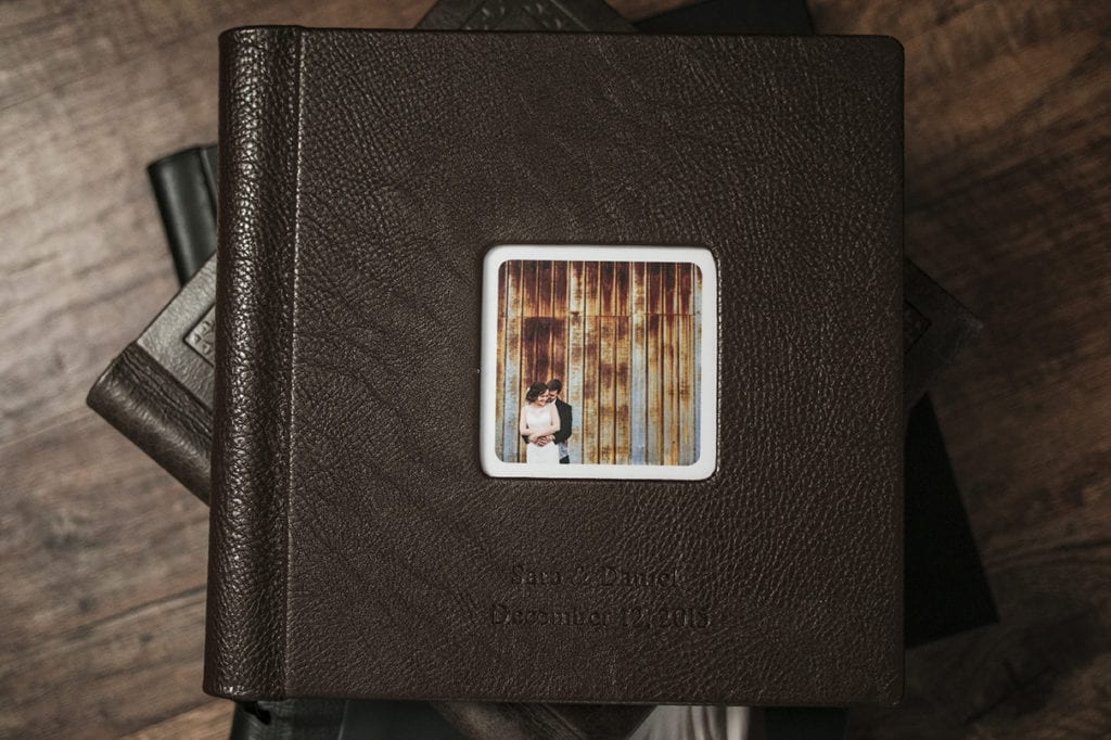 Embossed leather cover of Modern Ontario Wedding Album featuring couple cuddling in front of rusted metal wall