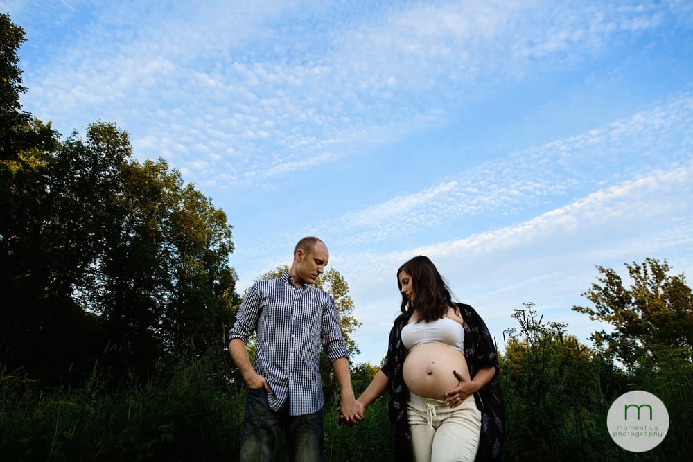 pregnant woman against blue sky holding husband's hand