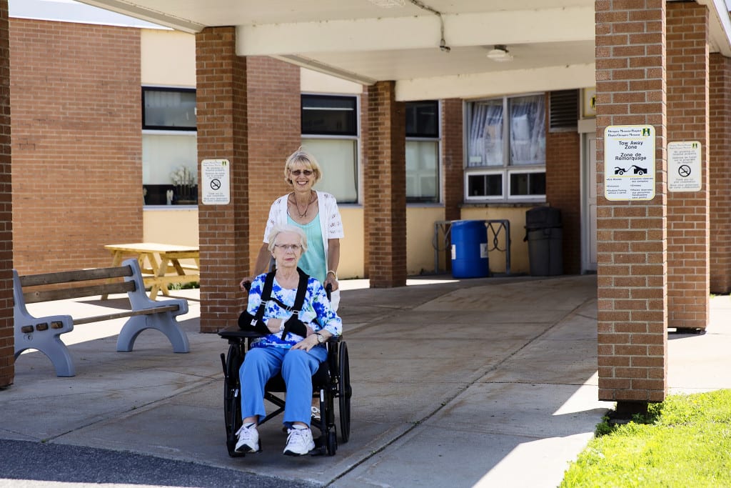 daughter pushing mother in wheelchair out of hospital