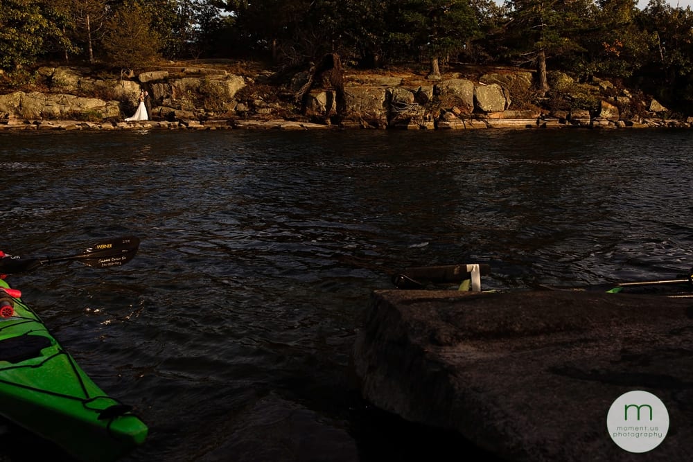 bride and groom on rocks with kayakers