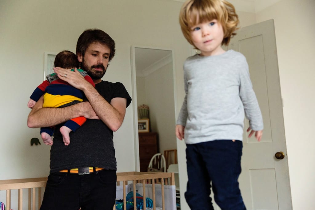 London dad holding son while boy jumps on bed