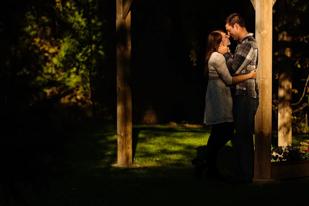 Ontario wedding photographer - couple cuddling for Cornwall engagement photos next to wooden frame