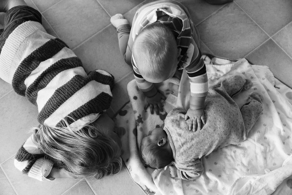 Cornwall family photographer - sisters on kitchen floor with newborn
