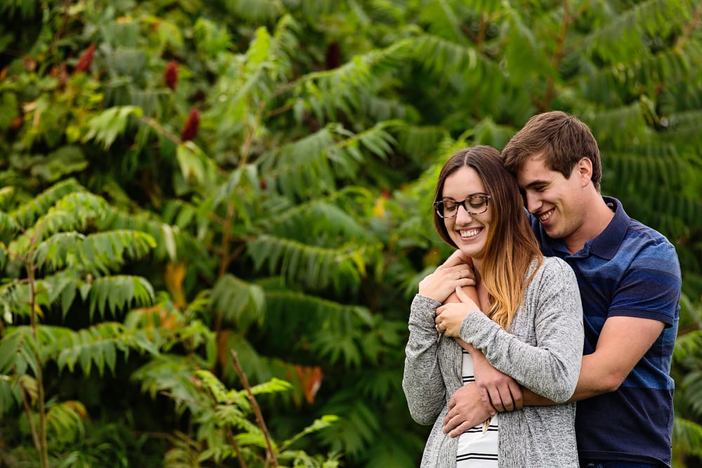 Ontario wedding photographer - couple cuddling for Cornwall engagement photos in front of sumac