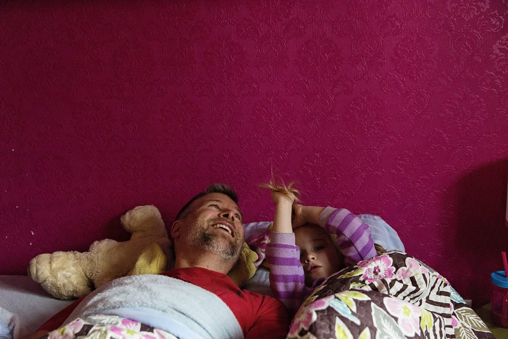 dad and daughter in bed with pink wall