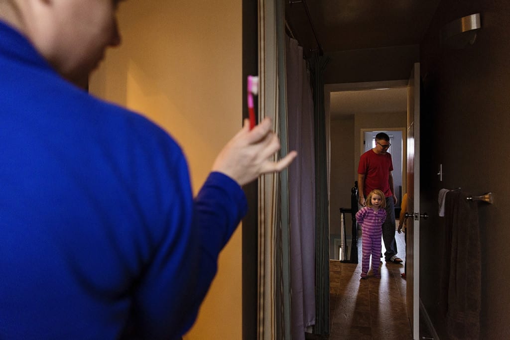 Mom holding toothbrush daughter looking uncertain