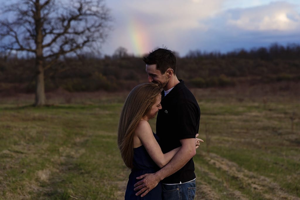 laughing in field with rainbow during Cornwall engagement session
