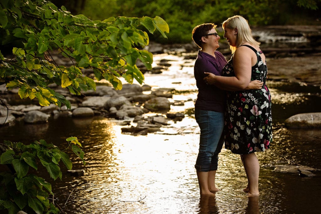 Women embracing in shallow river at sunset