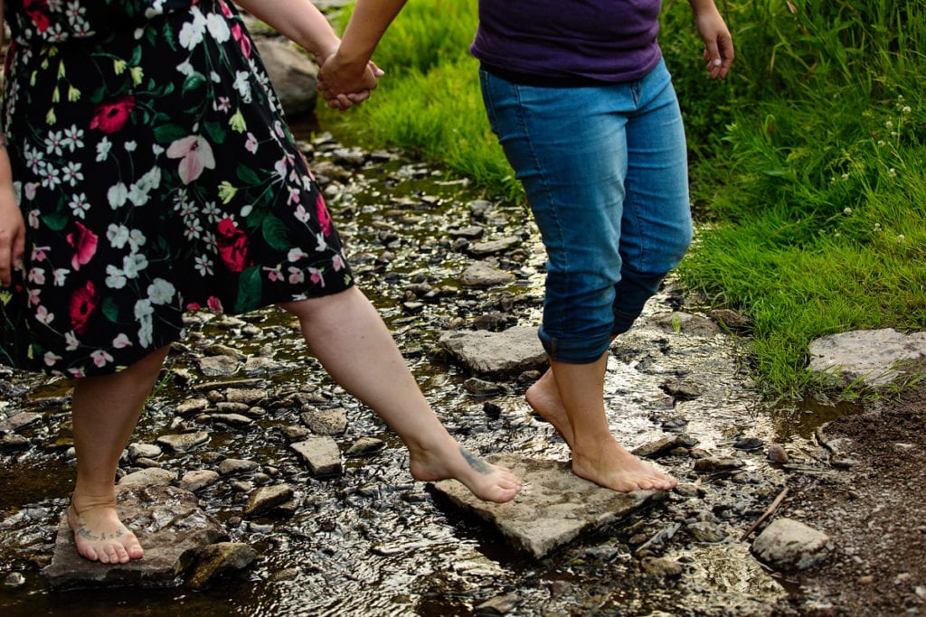 Couple holding hands and rolled up jeans in creek
