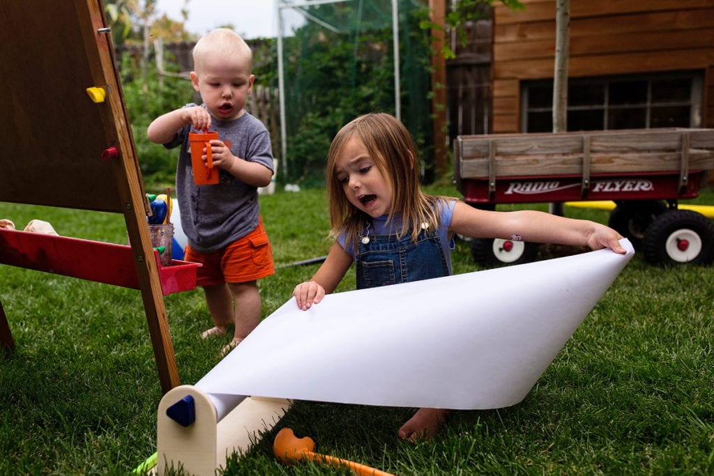 Siblings with roll of paper in backyard