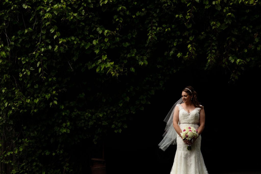 Bride in lace mermaid gown with bouquet in front of lush greenery