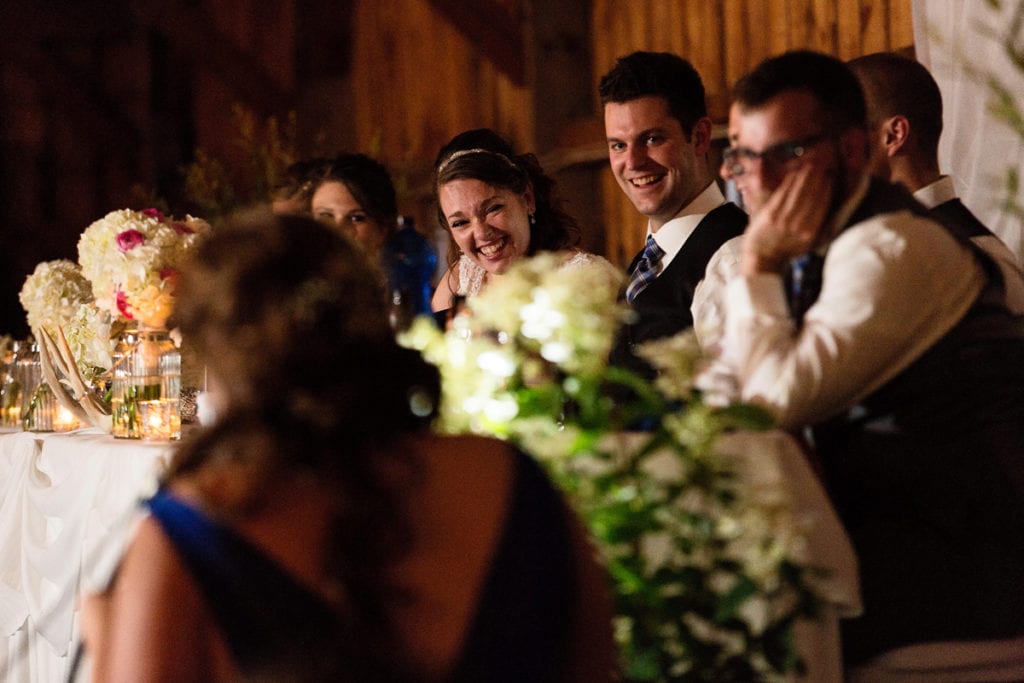 Bride and groom laughing with wedding party at head table