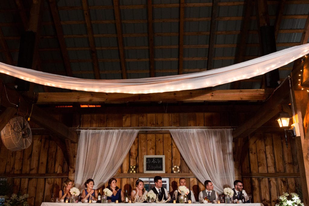 Head table with wedding party in rustic barn wedding venue