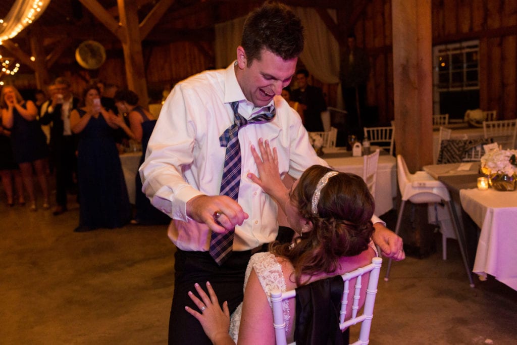 Garter toss with bride on white chiavari chair and groom with crooked tie