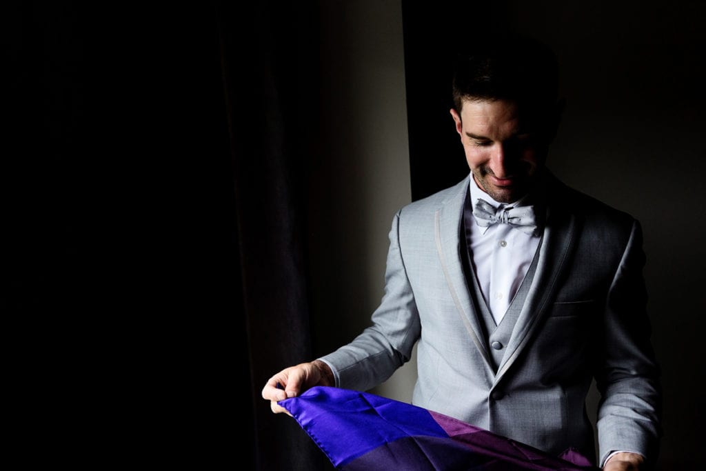 Groom in grey suit folding blue and purple pocket square
