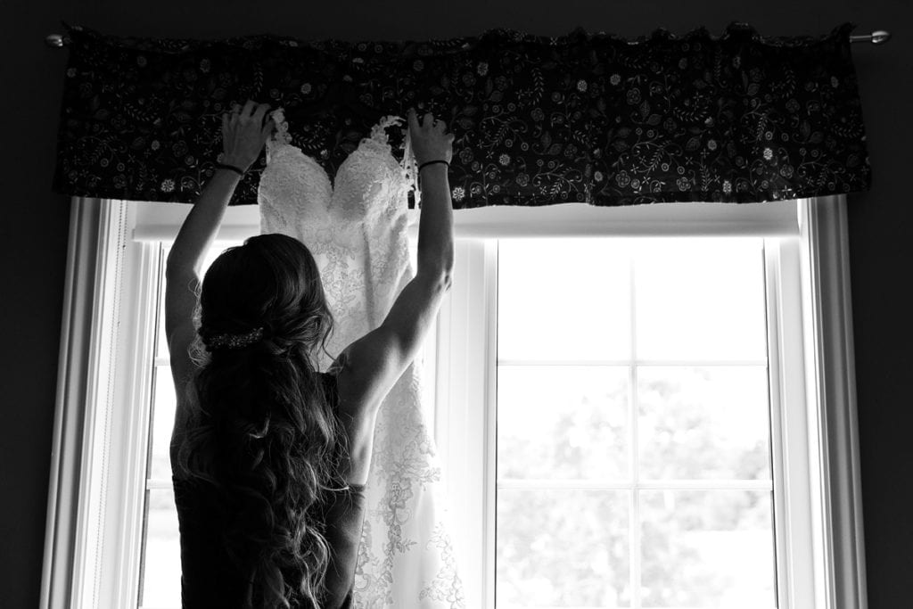 Bride hanging up wedding dress in front of window