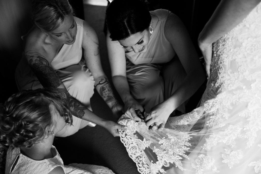 Bridesmaids helping bride with wedding gown and getting ready