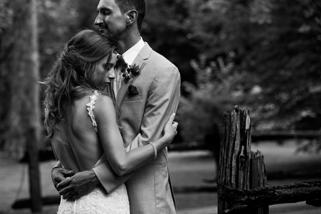 Bride ad groom embracing beside rustic wooden fence at intimate Strathmere wedding