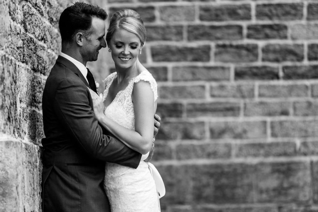 newly married groom holding his new bride against stone wall