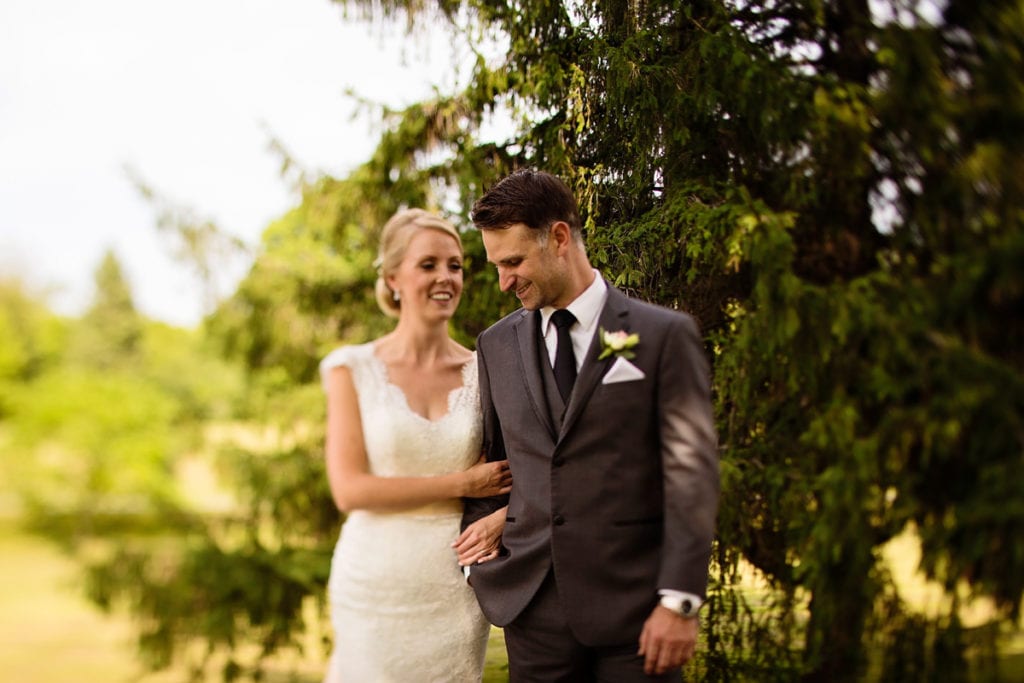 Bride in lace dress and groom in grey suit walk arm in arm