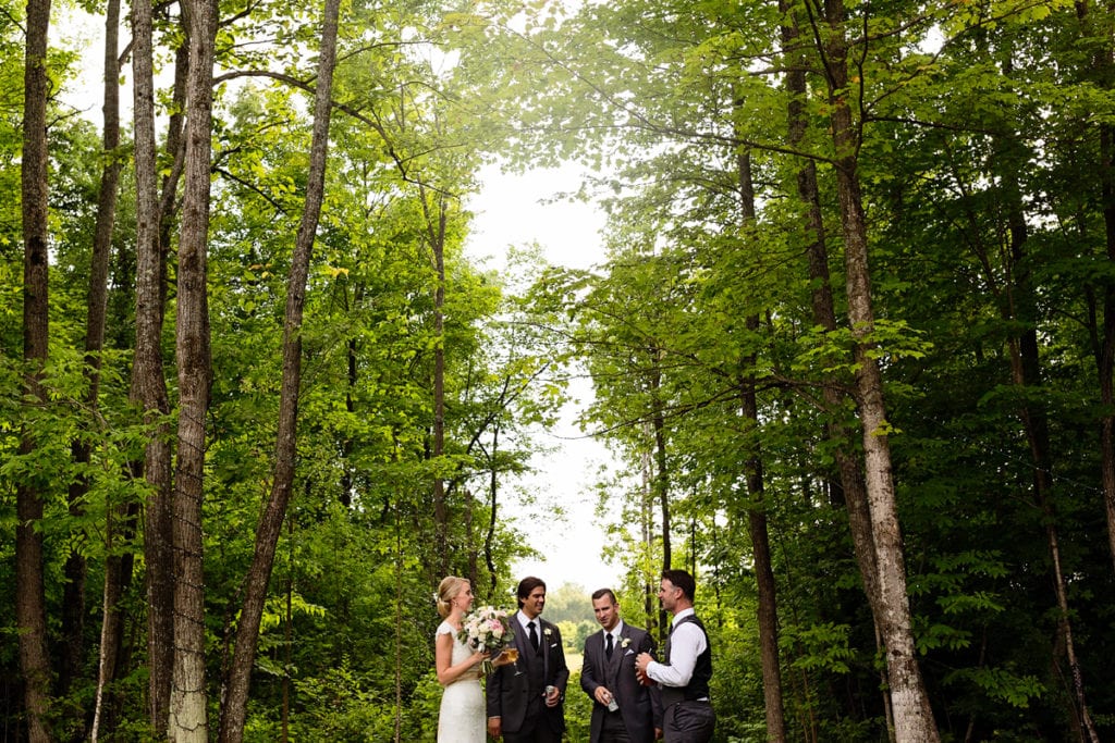 Bride and groom with best man and usher having drinks in wooded area