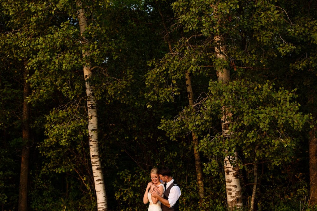 Groom holding bride in poplar tree stand at sunset