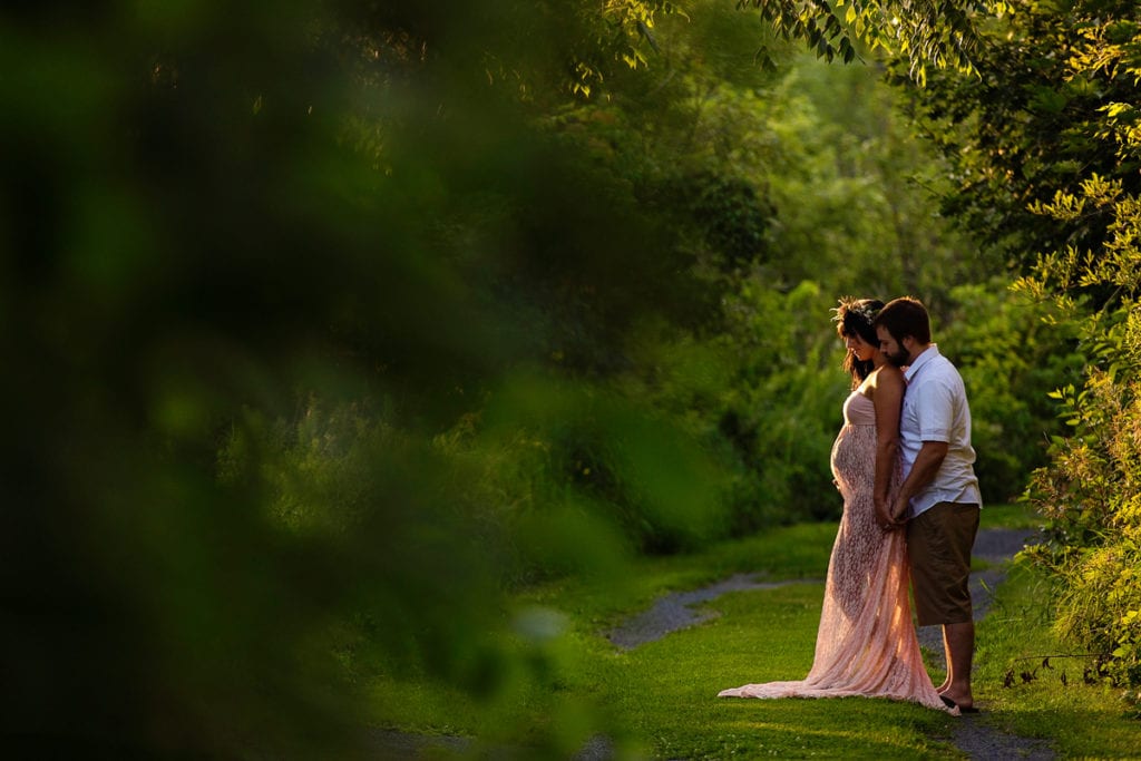 Bohemian pregnant woman on nature trail with husband standing behind her