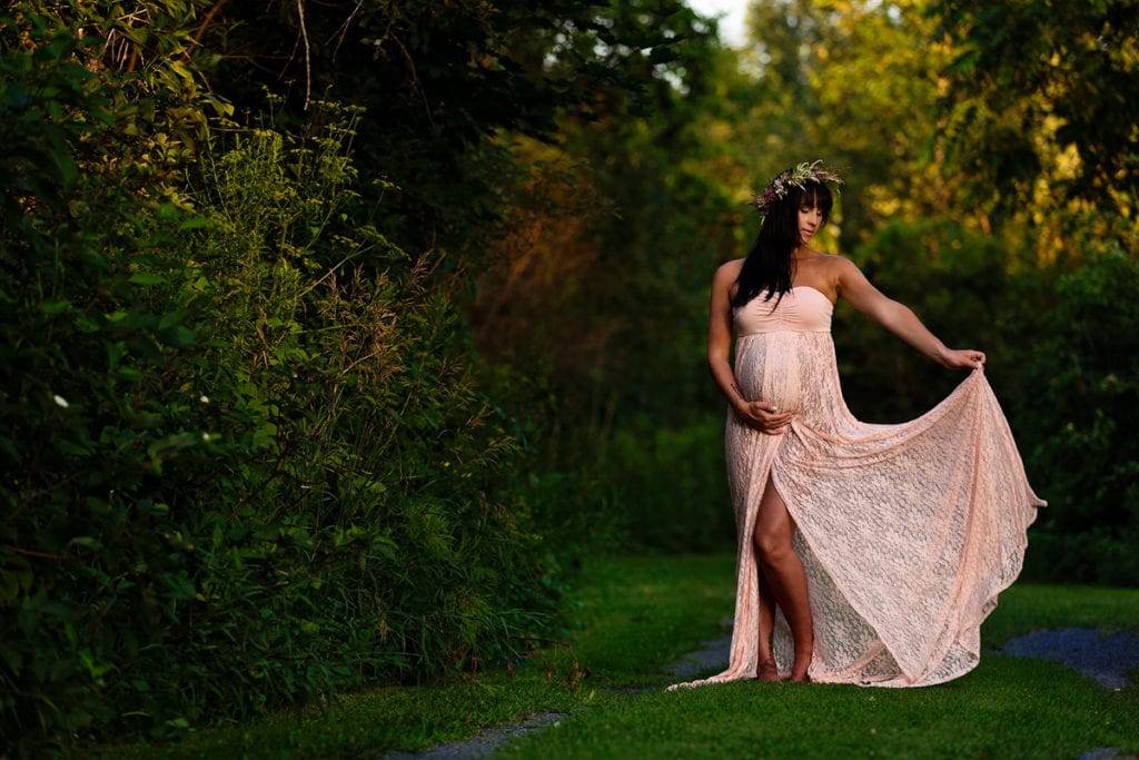 Bohemian pregnant woman in floral crown on lush green path