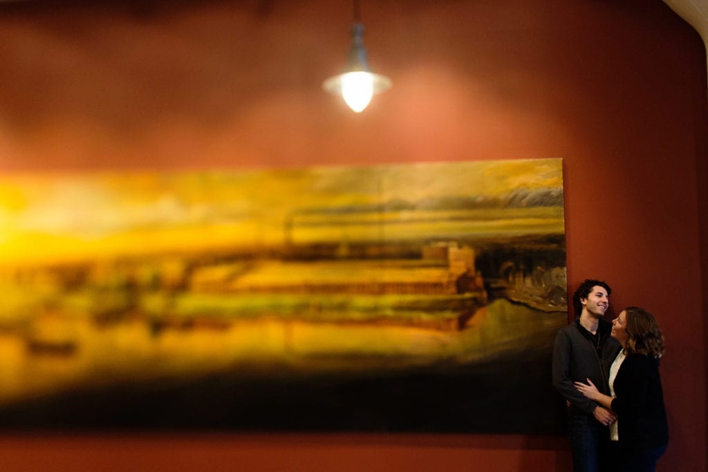 Engagement photo of smiling couple with gallery painting and industrial light