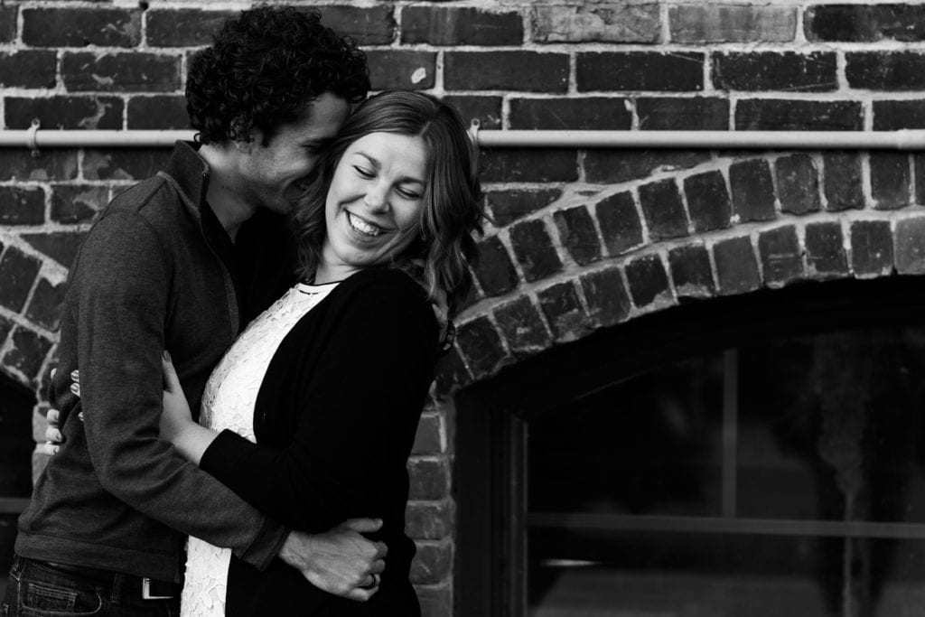 Couple laughing in front of brick building in urban Cornwall engagement session