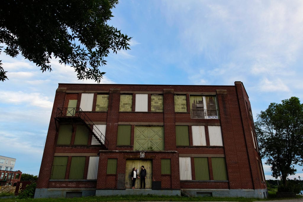 Couple holding hands in front of industrial building in modern urban engagement shoot