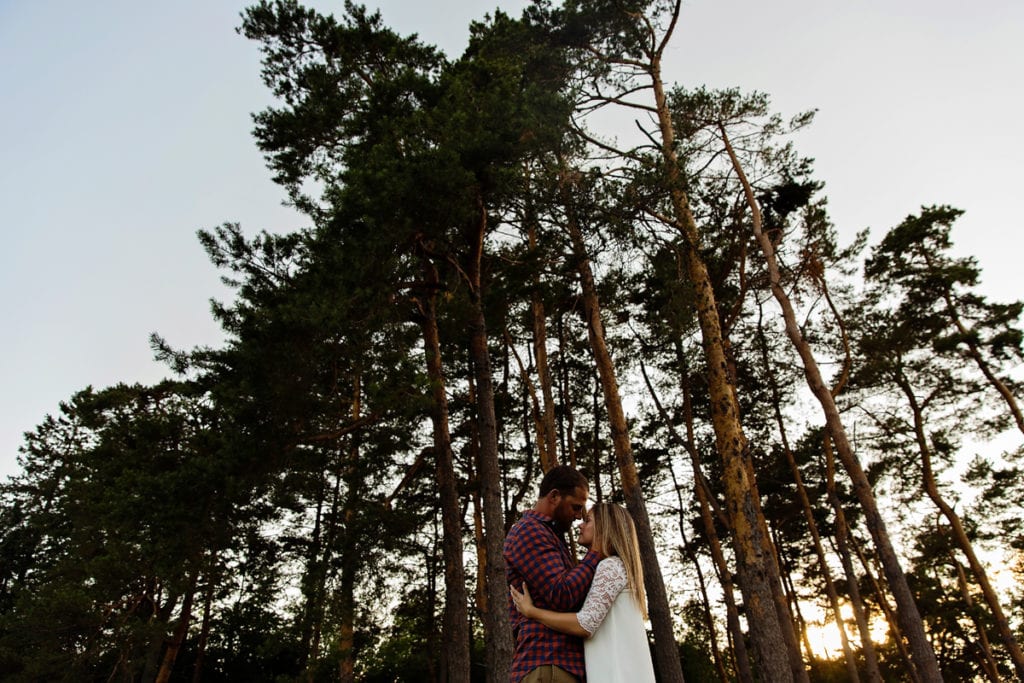 Man holding fiancee in front of tree stand in Rural Cornwall engagement session