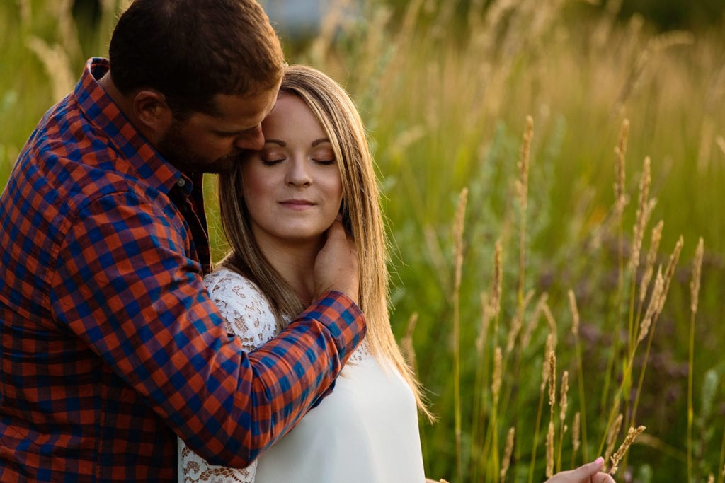 Man in plaid shirt with arm around fiancee in tall grass