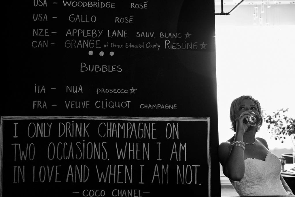 bride wearing fascinator with champagne quote on wall