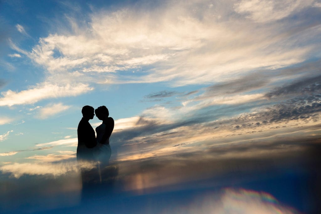 silhouetted brides against cloudy summer sky with reflection
