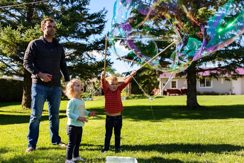 little girl and brother playing with soap bubble wands in backyard