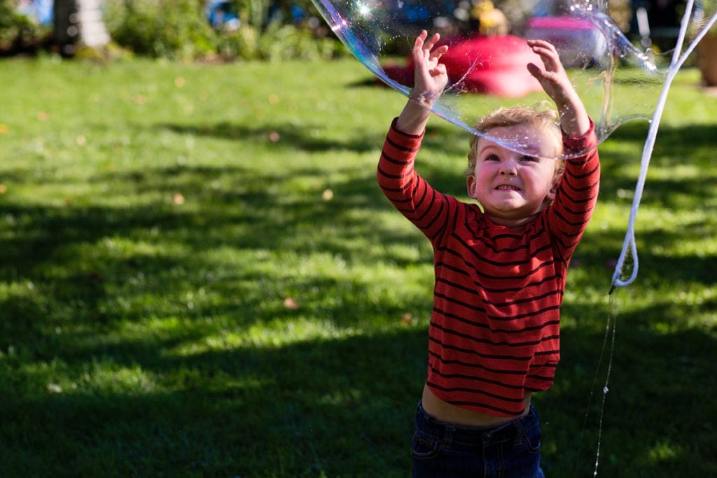 little boy making funny face while popping large soap bubbles