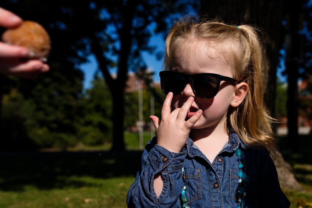 cool looking little girl wearing sunglasses licking her fingers during picnic in the park