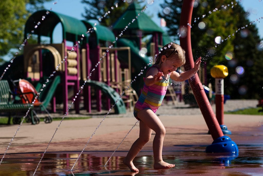 little girl in brightly coloured bathing suit playing in splash park
