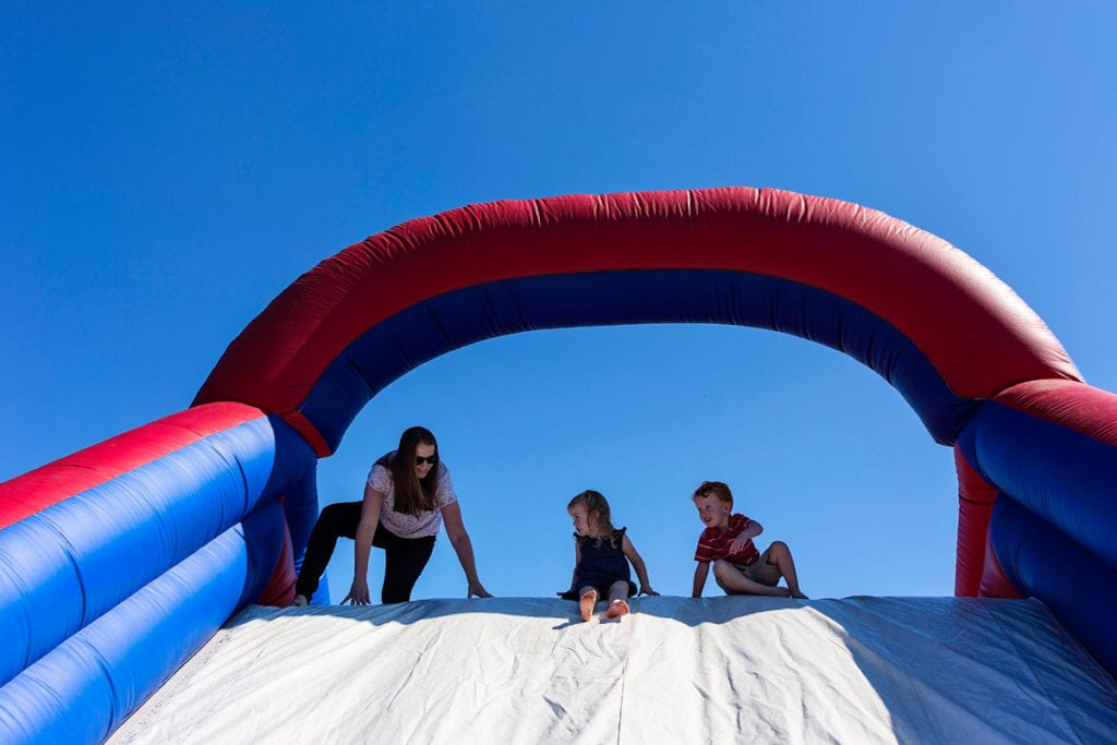 Mom sliding down inflatable slide with boy and girl