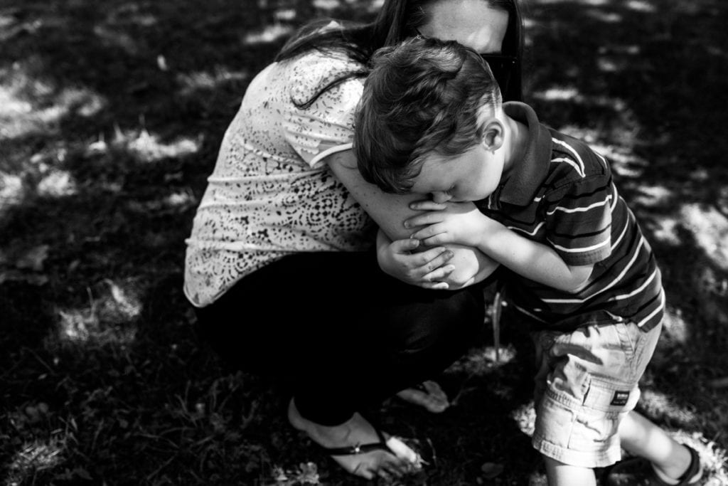 little boy in striped shirt and shorts being comforted by mom