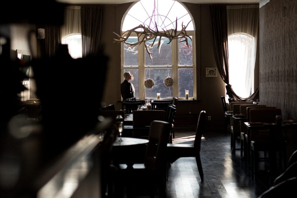 bride in suit looking out window at trendy restaurant wedding