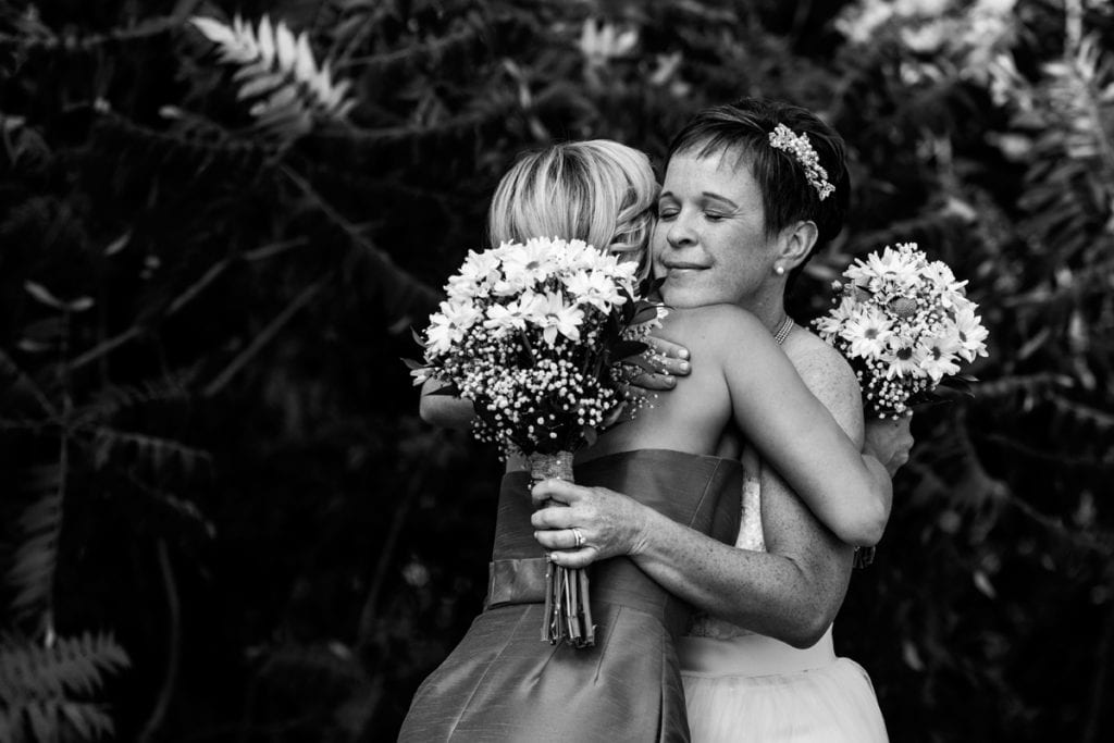 bride and bridesmaid hugging holding bouquets of daisies